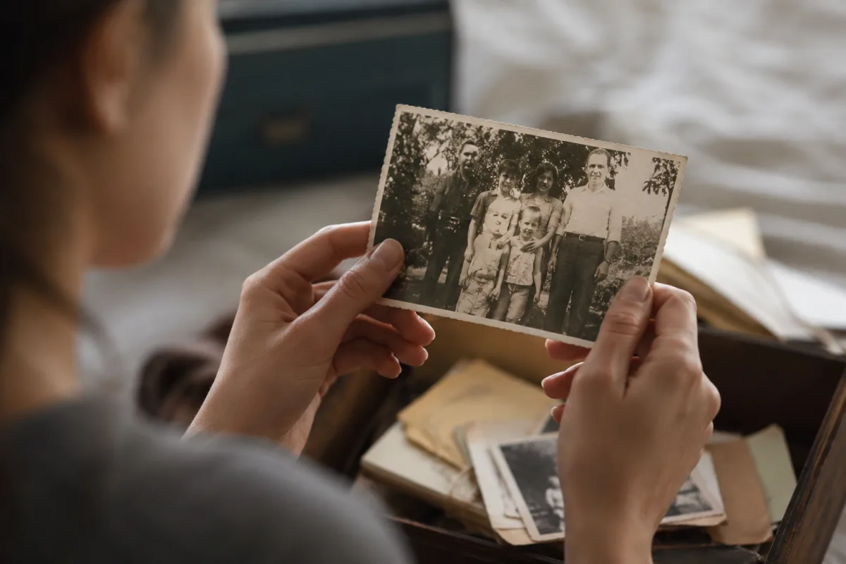 La dette transgénérationnelle : ce poids invisible qui se transmet dans ton corps et ta vie Mains d'une femme tenant un album de photos jauni ouvert sur un portrait de famille ancien
