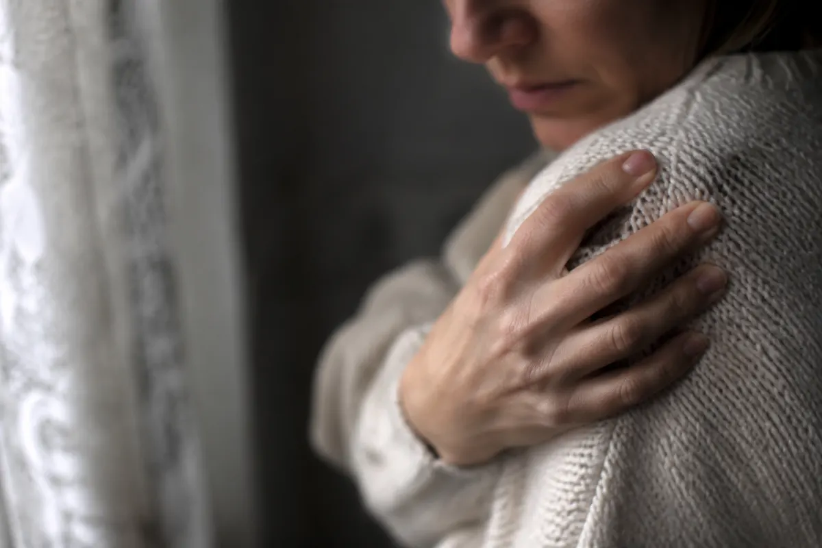 Symptômes d'un deuil non fait : ce que ton corps et ta tête tentent de te dire Main de femme posée sur une vieille photo en noir et blanc, lumière douce et floue en arrière-plan
